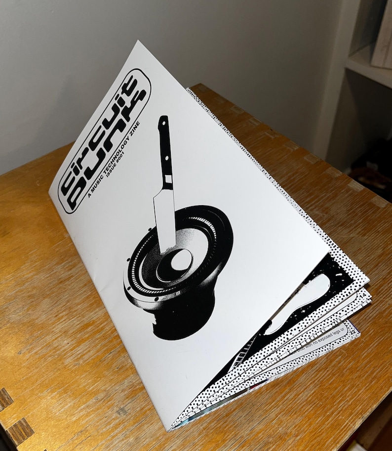 May include: A black and white magazine cover with the title "Circuit Blips" and the text "A Music Technology Zine Issue #001". The cover features a black and white illustration of a speaker with a knife sticking into it.