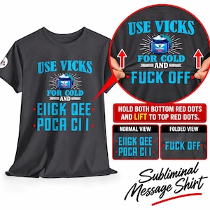 May include: A dark gray short-sleeved t-shirt featuring a graphic of a Vicks VapoRub jar with the text USE VICKS FOR COLD AND EIIGK QEE POCA CI I. The design includes a folding mechanism that reveals the hidden text FUCK OFF when lifted.