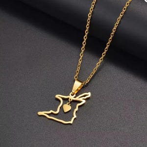 以下が含まれることがあります： トリニダード・トバゴの形をしたペンダントが付いたゴールドカラーのネックレス。小さなハートのチャームが付いています。チェーンとペンダントは光沢のある金属素材で作られています。ネックレスは暗い背景に表示されています。