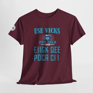 May include: A maroon t-shirt with the text "USE VICKS FOR COLD AND" in blue with a blue and white illustration of a Vicks VapoRub container. The text "EIGK QEE" and "POCA CII" are also in blue.