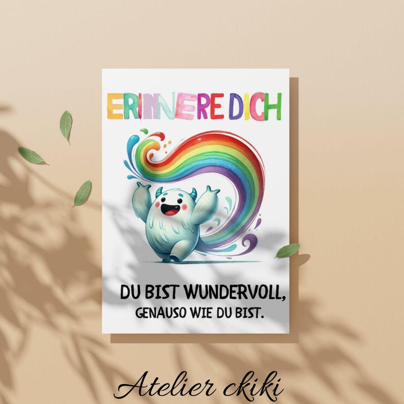 May include: A white card with a cartoon monster and a rainbow design. The card has the text "ERINNERE DICH" at the top and "DU BIST WUNDERVOLL, GENAUSO WIE DU BIST" below the monster. The card also has the text "Atelier ckiki" at the bottom.