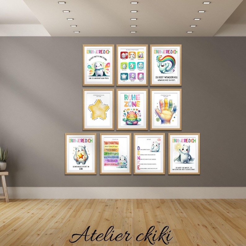 May include: A collection of framed art prints with whimsical illustrations and text. The prints feature colorful designs, including a star, handprints, and cartoon characters. The artwork is displayed on a gray wall above a wooden floor.