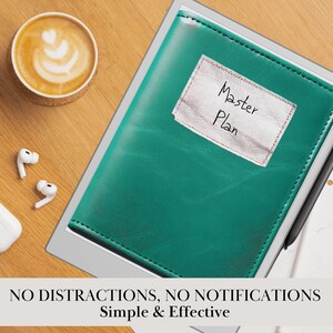 May include: A green leather notebook with a white label that says "Master Plan" on it. The notebook is on a white surface with a cup of coffee and earbuds.