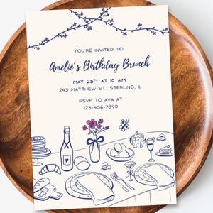 Könnte beinhalten: Eine weiße Einladungskarte mit blauem und violettem Text und Illustrationen. Der Text lautet "Sie sind eingeladen zum Geburtstagsbrunch von Amelie, am 25. Mai um 10 Uhr, 243 Matthew St, Sterling, IL, RSVP an Ava unter 123-456-7890". Die Illustration zeigt ein Gedeck mit einer Blumenvase, einer Weinflasche, Tellern und Besteck.