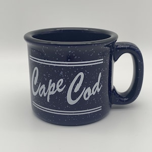 Op de afbeelding: Een blauwe keramische mok met witte stippen en de tekst "Cape Cod" in witte letters.