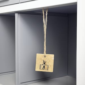 May include: A brown tag with a black and white illustration of a diffuser hanging from a string in a gray cabinet.