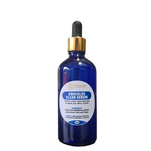 May include: A cobalt blue serum bottle with a gold dropper. The label reads "KNUCKLES CLEAR SERUM" and lists ingredients. The product is designed to clear dark spots on hands, feet, elbows, and knees. The bottle is filled with a clear liquid.