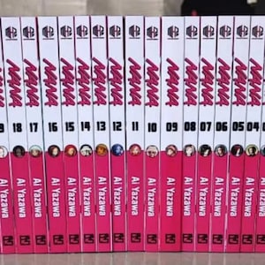 Op de afbeelding: Een complete set van 21 manga-volumes van "NANA" door Ai Yazawa. De ruggen zijn wit met zwarte tekst en een roze streep. De omslagen bevatten illustraties van de personages.