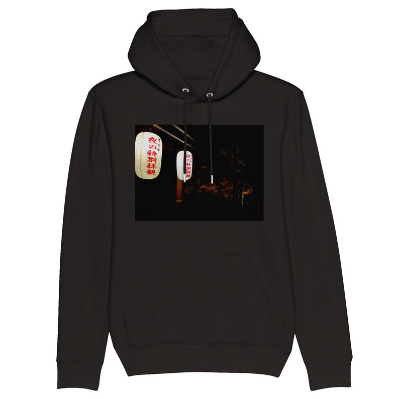 Pu&ograve; includere: Felpa con cappuccio nera con una grafica bianca di lanterne giapponesi appese al buio. Le lanterne hanno un testo rosso che dice "夜のお神輿" che si traduce in "Night Mikoshi".