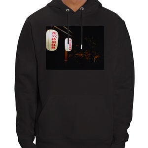 Pu&ograve; includere: Felpa con cappuccio nera con una grafica di due lanterne giapponesi bianche con testo rosso. Il testo sulle lanterne dice "夜のお祭り", che si traduce in "Festival notturno".