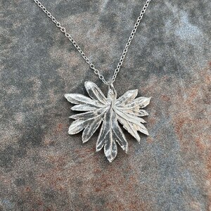 May include: A silver necklace with a detailed leaf pendant. The pendant is made of metal and has a delicate, intricate design.