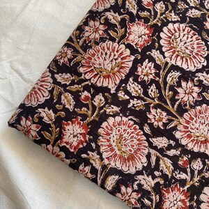 May include: Black fabric with a floral print in shades of pink, red, and gold. The fabric has a textured surface and a repeating pattern of large and small flowers.