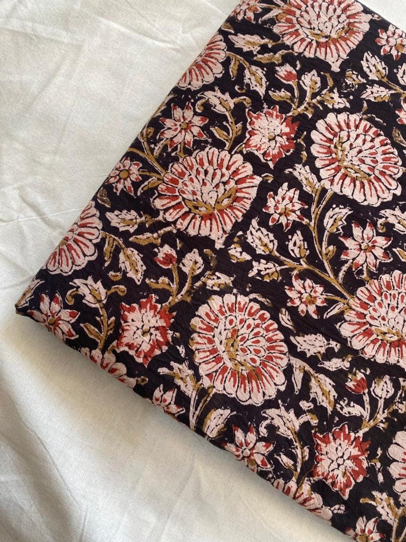 May include: Black fabric with a floral print in shades of pink, red, and gold. The fabric has a textured surface and a repeating pattern of large and small flowers.