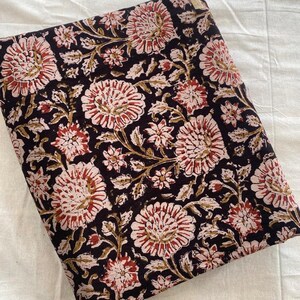 May include: A black fabric with a floral print in shades of pink, red, and brown. The fabric is folded in half and has a small white tag on the top right corner.