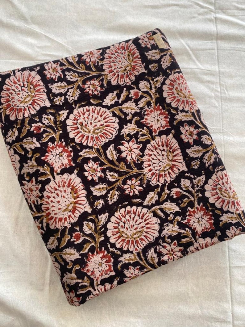 May include: A black fabric with a floral print in shades of pink, red, and brown. The fabric is folded in half and has a small white tag on the top right corner.