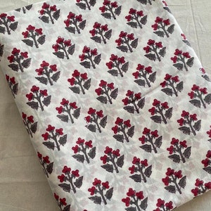 Puede incluir: Tela de algodón blanca con un patrón repetido de pequeñas flores rojas con tallos y hojas grises.