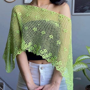 Peut inclure: Un châle en crochet vert citron présentant un motif en maille ajourée avec de petits motifs floraux. Le vêtement possède un ourlet asymétrique en pointe et est porté sur un haut bandeau noir et un jean en denim clair.