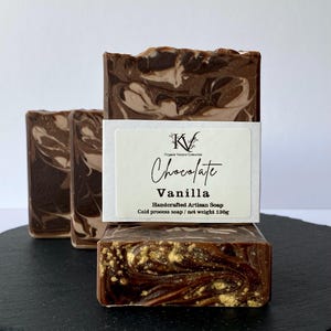 Puede incluir: Tres jabones artesanales hechos a mano con un diseño de remolino de chocolate y vainilla. Los jabones son de color marrón oscuro con acentos marrones claros y dorados. El jabón delantero tiene una etiqueta que dice "Chocolate Vanilla".