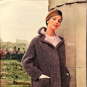 May include: A woman wearing a long, gray, fuzzy coat with a white collar and pockets. She is standing next to a stone wall. The text "No. 4914 Instructions on page 31" is visible in the bottom right corner of the image.