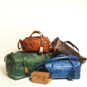 Peut inclure: Plusieurs sacs de voyage en cuir de différentes couleurs, dont marron, vert et bleu. Les sacs ont des poignées, des fermetures éclair et des étiquettes de bagages. Une petite trousse de toilette marron est également présente.
