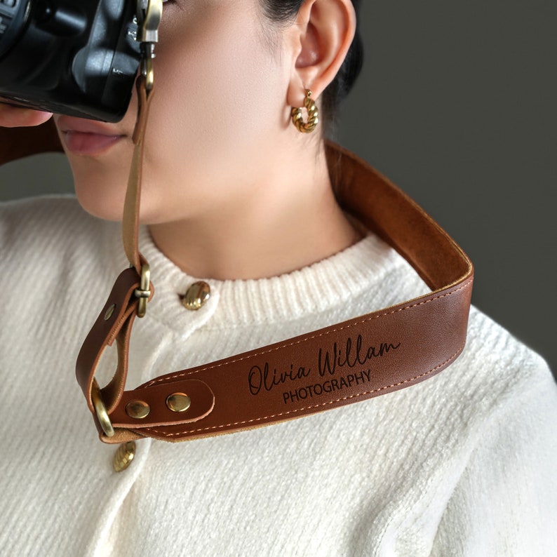 May include: A brown leather camera strap with the text "Olivia William PHOTOGRAPHY" engraved in gold lettering.