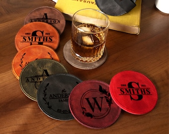 May include: Six round leather coasters with personalized engravings. The coasters feature various designs including names, dates, and initials. The coasters are brown, green, red, and black.