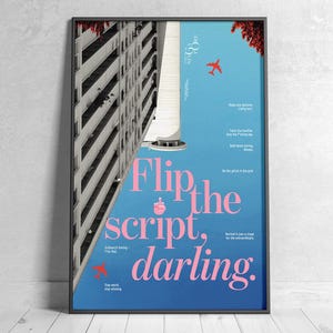 May include: Framed poster with a blue background and the words "Flip the script, darling" in pink. The poster features a building and a red airplane graphic. The poster is displayed on a white wooden floor.