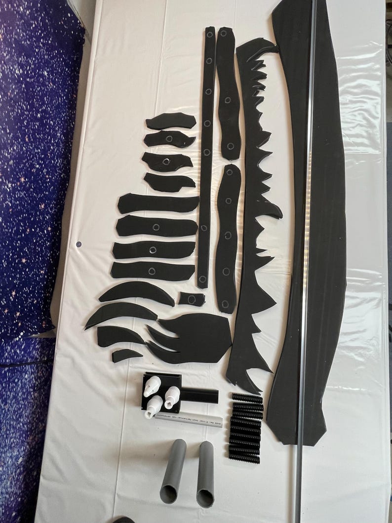 May include: A set of black foam pieces for crafting a dragon costume. The set includes a long, thin piece of foam, a long, curved piece of foam, and several smaller pieces of foam. There are also white plastic pieces, black plastic pieces, and gray PVC pipes.