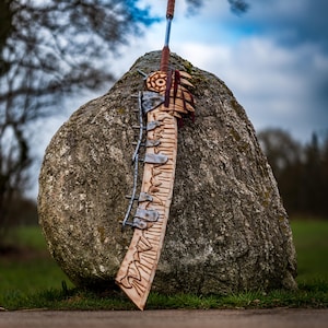May include: A large, wooden sword with a metal blade and a leather handle. The sword is leaning against a large rock.