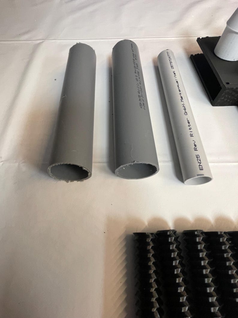 May include: Three gray PVC pipes with printed text on the side. The text on the pipe on the right reads "EN25 Rev Ritter GmbH-Markenmanual | L.Nr. 05732477".