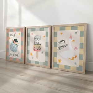 May include: Three framed art prints with playful illustrations. One shows a ladybug in a blue polka-dot blanket with the text "snug as a bug." Another features an ice pop with "cool kids club." The last print has a goose wearing a party hat with "silly goose."