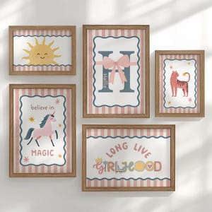 May include: A collection of five framed art prints with a playful theme. The prints feature a smiling sun, a unicorn, a tiger, a letter "H" with a bow, and the words "Long Live Girlhood". The frames have a wood effect finish.