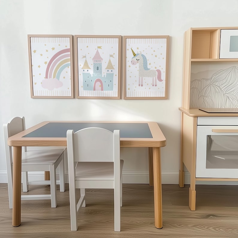 Pu&ograve; includere: Un'area giochi per bambini con un tavolo in legno, piano grigio e due sedie bianche. Sopra, tre stampe incorniciate raffigurano un arcobaleno, un castello e un unicorno. A destra c'&egrave; una cucina giocattolo in legno. Il tavolo &egrave; lungo circa 76 cm.