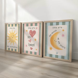 May include: Three framed art prints with a light wood finish. Each print features a different design with the words "you are" at the top. One print has a smiling sun, another has a heart, and the last has a crescent moon.