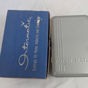 May include: A vintage Intermatic timer and its original blue box. The box has the Intermatic logo and the text "Controls for Home, Industry and Commerce." The timer is silver with the text "INTER-MATIC."