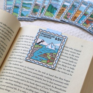May include: A collection of rectangular paper bookmarks designed to look like postage stamps, featuring colourful illustrations of various landscapes. One bookmark is placed inside an open book, depicting a puffin, iceberg, and the text Newfoundland & Labrador 65p.