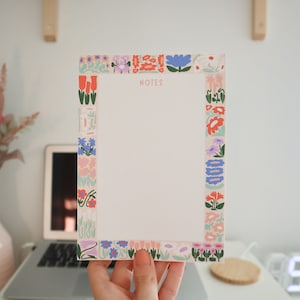 May include: A white notepad with a floral border in shades of pink, blue, green, and orange. The notepad has the word "NOTES" printed at the top.