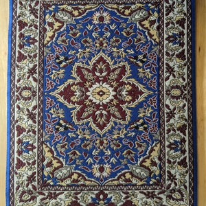 May include: A small, blue and cream colored rug with a floral pattern. The rug has a fringe border.