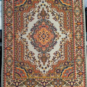 Peut inclure: Un petit tapis rectangulaire avec un motif persan traditionnel. Le tapis a un fond crème avec des motifs complexes dans des tons de rouge, orange, jaune, noir et bleu.