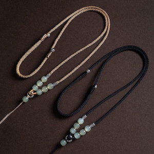 May include: Two necklaces with green jade beads and silver accents. One necklace has a brown cord and the other has a black cord.
