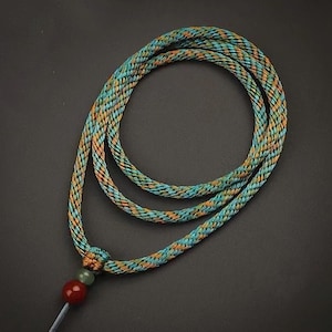 Peut inclure: Un collier en cordon tressé bleu et or avec une perle rouge et verte à l'extrémité.
