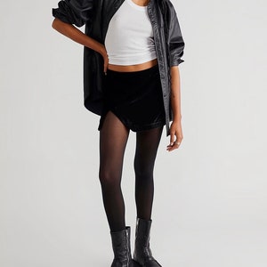 May include: A black velvet mini skirt with a side slit and a high waist. The skirt is paired with black tights and black leather boots.