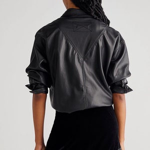 May include: A black faux leather shirt with a pointed collar and long sleeves. The shirt has a patch on the back with an embroidered 'X'. The model is also wearing a black velvet mini skirt.