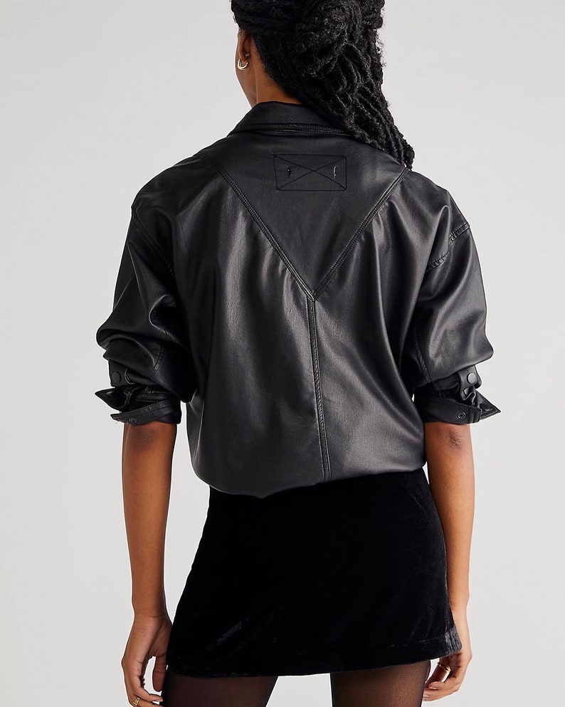 May include: A black faux leather shirt with a pointed collar and long sleeves. The shirt has a patch on the back with an embroidered 'X'. The model is also wearing a black velvet mini skirt.