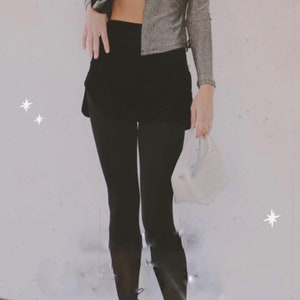 May include: A person wearing a silver sparkly top with a black skirt and black leggings. The person is holding a white mesh bag.