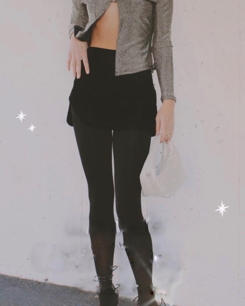 May include: A person wearing a silver sparkly top with a black skirt and black leggings. The person is holding a white mesh bag.