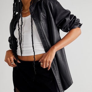 May include: A black faux leather shirt with a button-up front and a black velvet mini skirt. The skirt has a side panel of sheer fabric.
