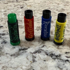 May include: Four cylindrical bottle stoppers, each with a black top and base. The stoppers are colored green, red, blue, and yellow, with the names of Hogwarts houses: Slytherin, Gryffindor, Ravenclaw, and Hufflepuff.