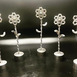 May include: Five silver metal flower sculptures with twisted stems and bases. Each flower is made of hexagonal nuts.