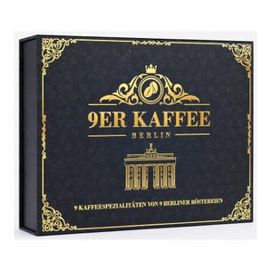 Könnte beinhalten: Eine rechteckige schwarze Schachtel mit Goldfolienakzenten. Die Vorderseite zeigt den Text 9ER KAFFEE BERLIN, eine Grafik des Brandenburger Tors und den Text 9 KAFFEESPEZIALITÄTEN VON 9 BERLINER RÖSTEREIEN. Der Hintergrund hat ein Kaffeebohnenmuster.
